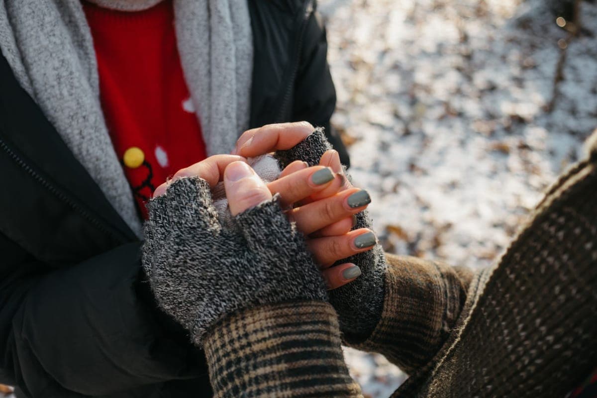 Two people holding hands in warm winter gloves on a snowy day