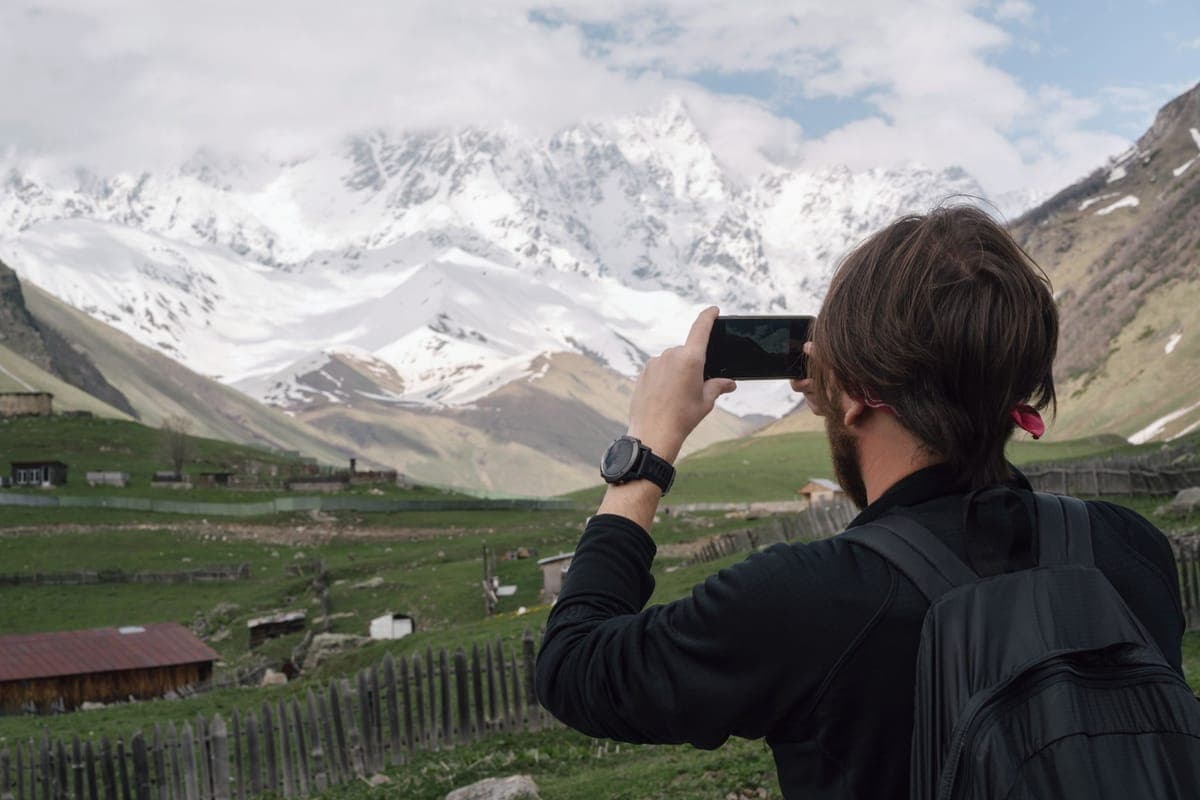 A person photographing a snowy mountain village on a winter day