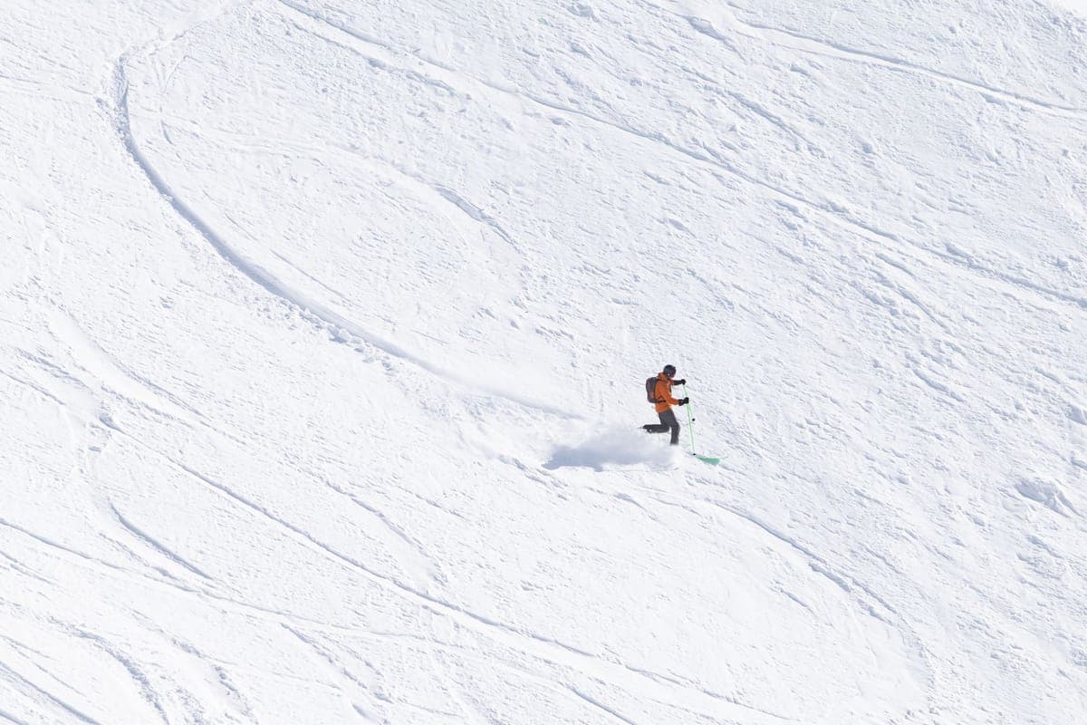 A skier descending a wide snow-covered mountain slope on a clear day