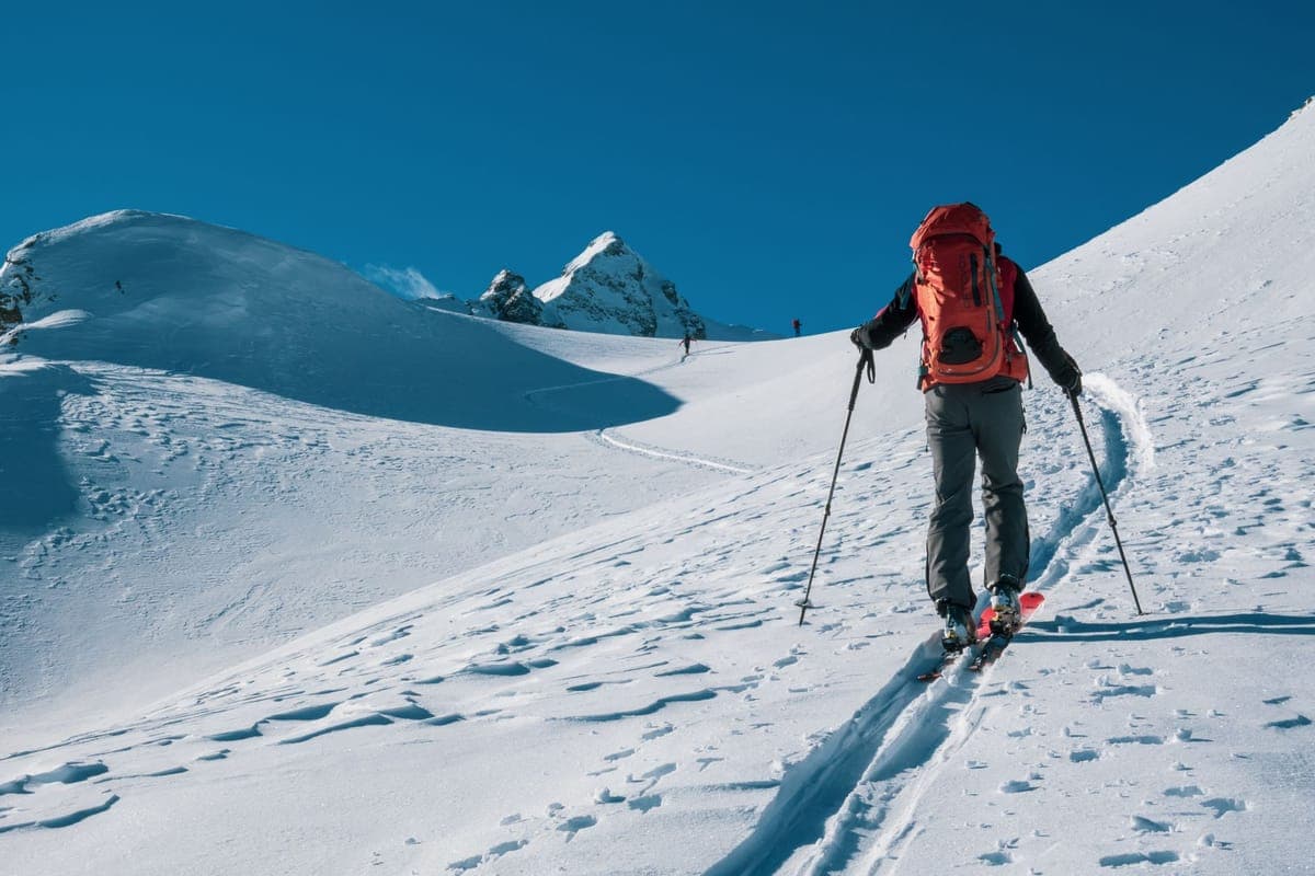 A person walking uphill through a snowy mountain landscape with equipment