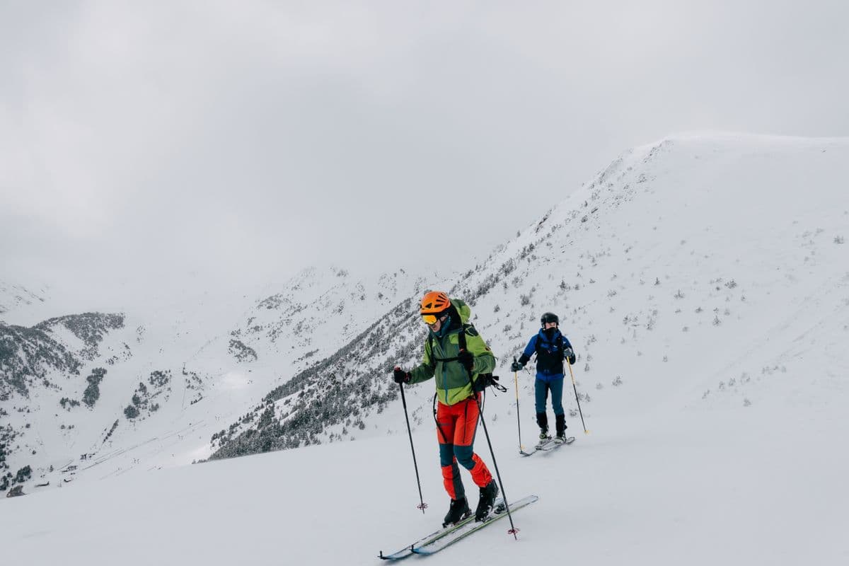 Two skiers in bright gear climbing a snowy mountain slope