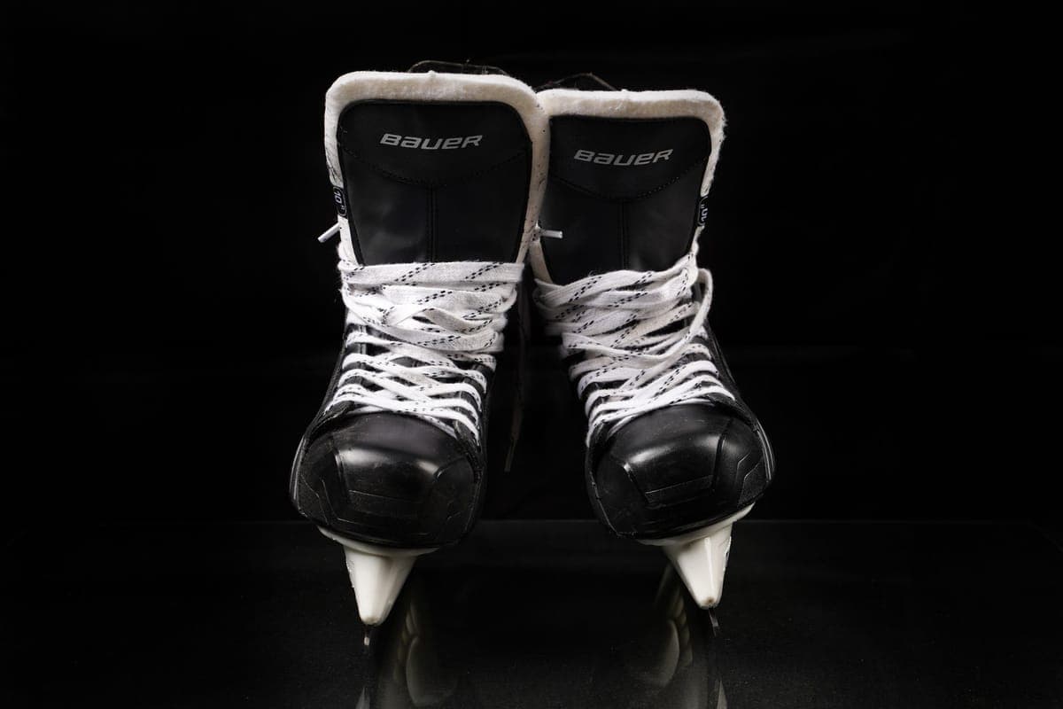 A pair of black ice skates with white laces on a dark background