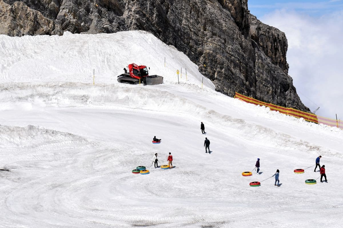 People riding a snow tube down a groomed hill on a sunny winter day