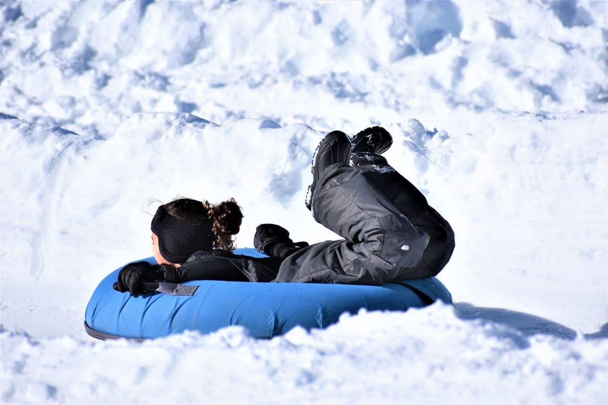 A child riding a snow tube down a snowy hill on a winter day