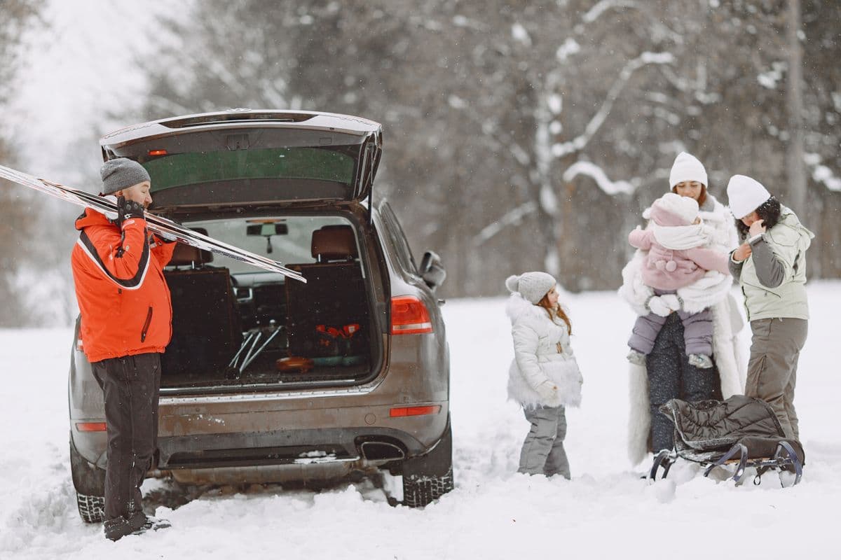 A family unloading skis and sleds from a car in a snowy landscape