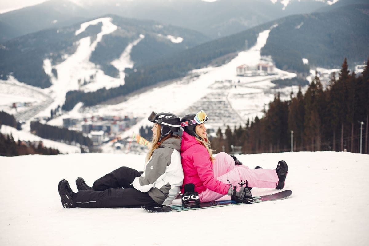 Two people sitting with snowboards on a snowy mountain slope