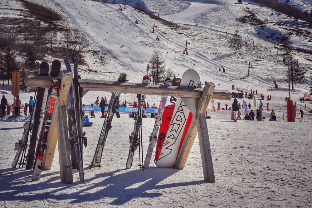 Skis and snowboards standing in the snow at a sunlit ski resort