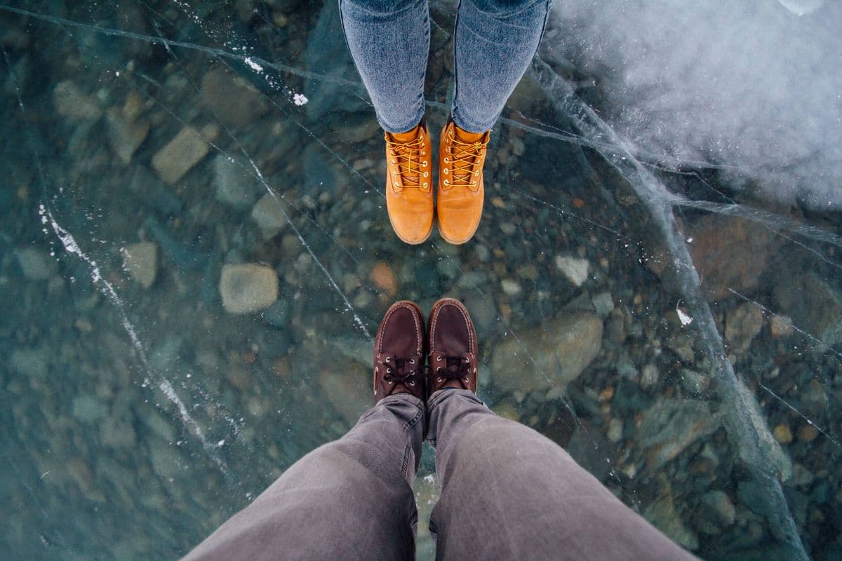 Two people standing on a frozen lake showing their winter boots and jeans