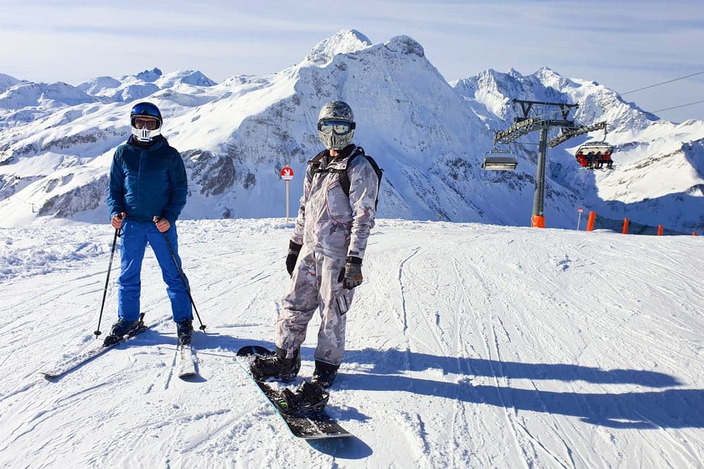 A skier and a snowboarder on a scenic winter mountain resort slope