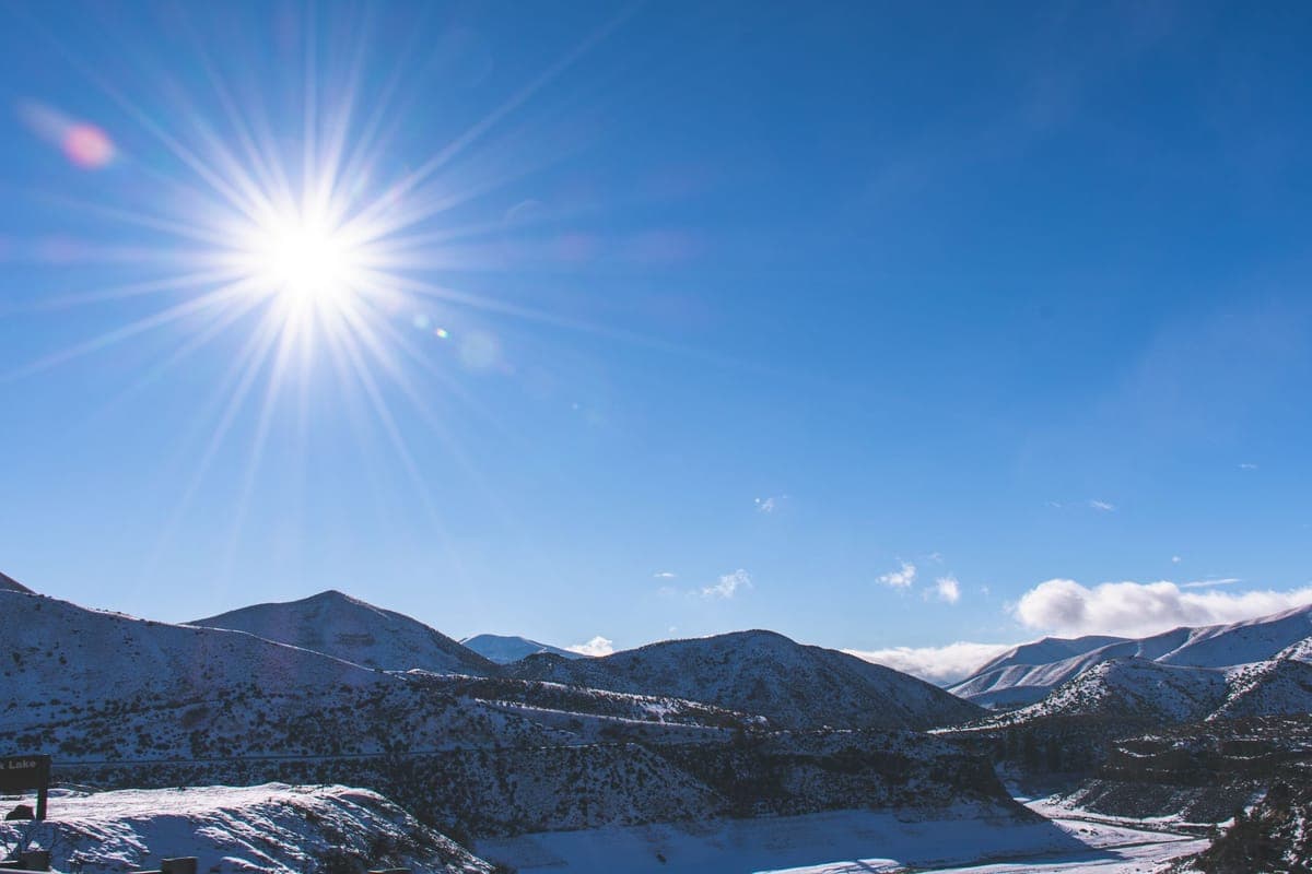A bright winter mountain landscape with sun over snow-covered peaks