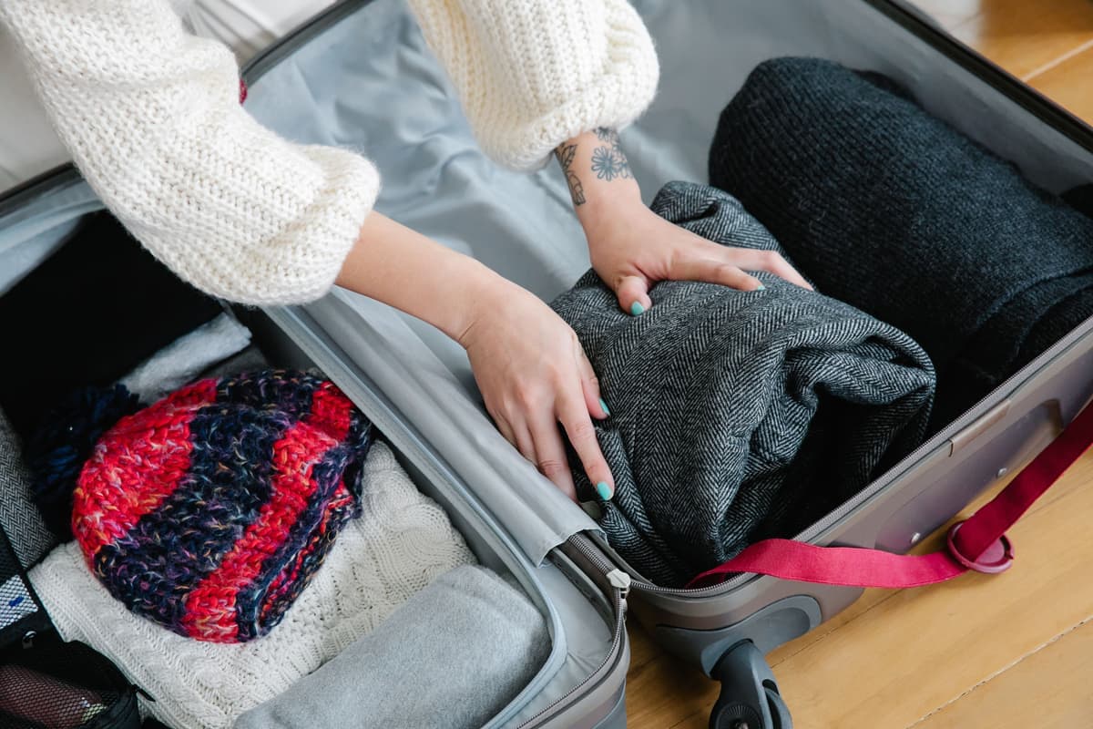 Hands packing knitwear into a suitcase for a trip