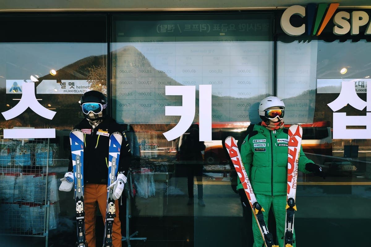 Skiers in winter clothing carrying skis outside a rental shop in the snow