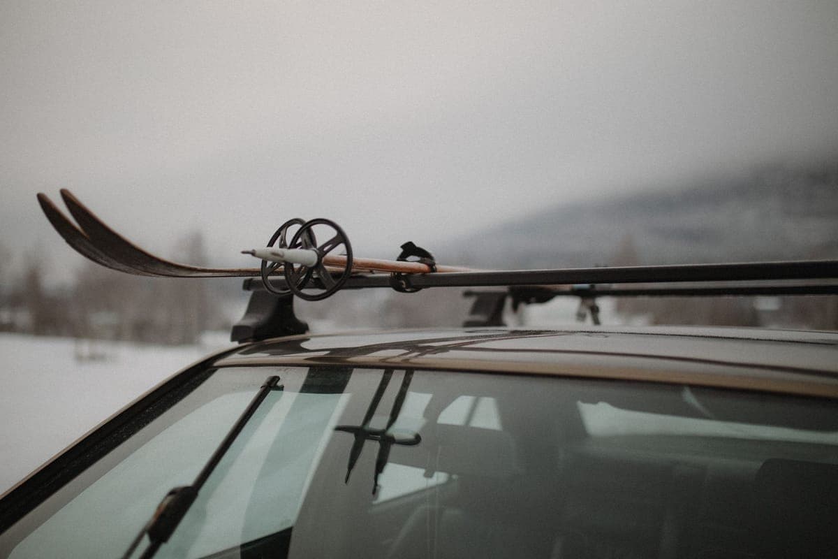 Skis and poles strapped to a car roof rack in a snowy winter setting