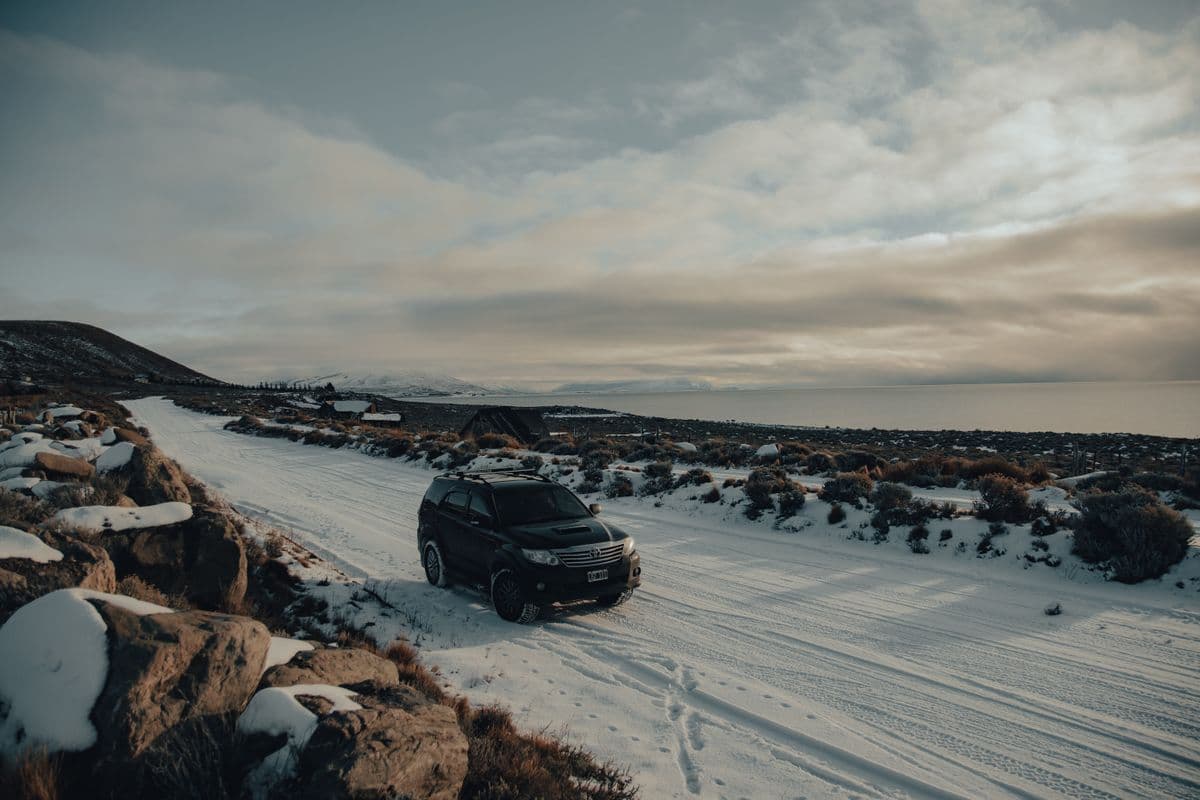A dark SUV driving along a snow-covered road through a winter landscape