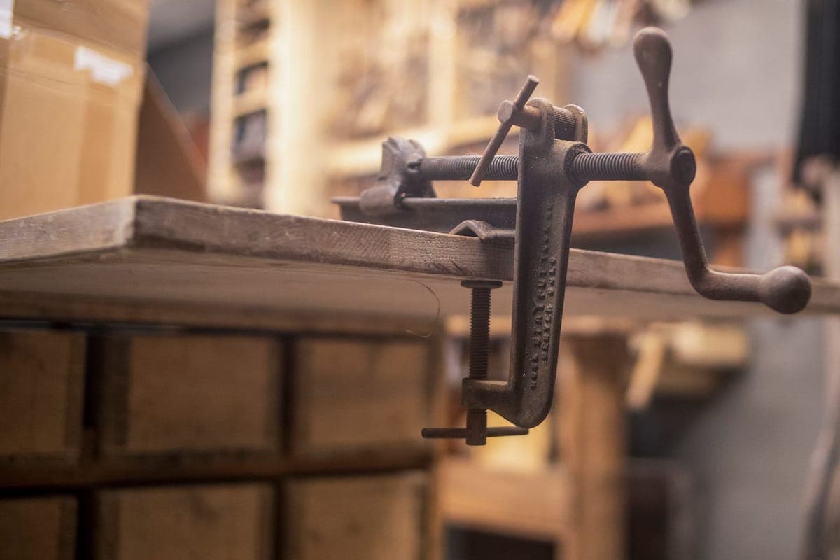 A close-up of a clamp fixed to a wooden workbench in a workshop
