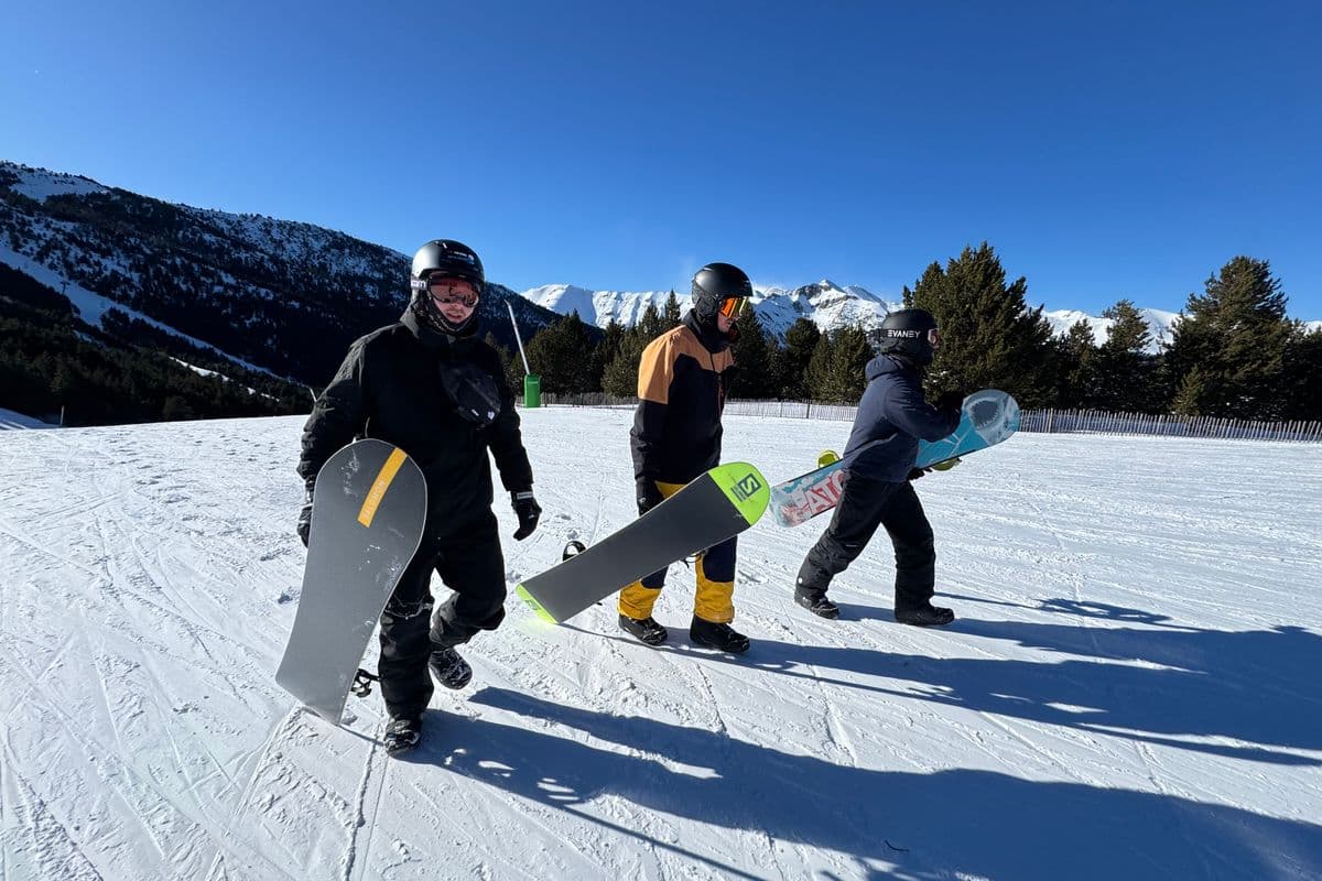 Three snowboarders walking across a snowy slope under a blue sky