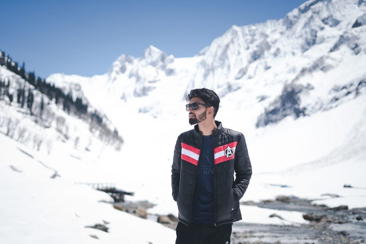 A man in a snowy mountain landscape wearing sunglasses and a winter jacket