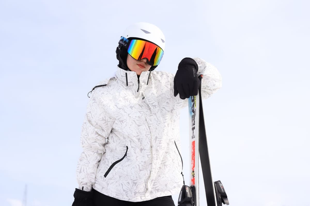 A skier in a helmet and goggles posing with skis against a snowy backdrop