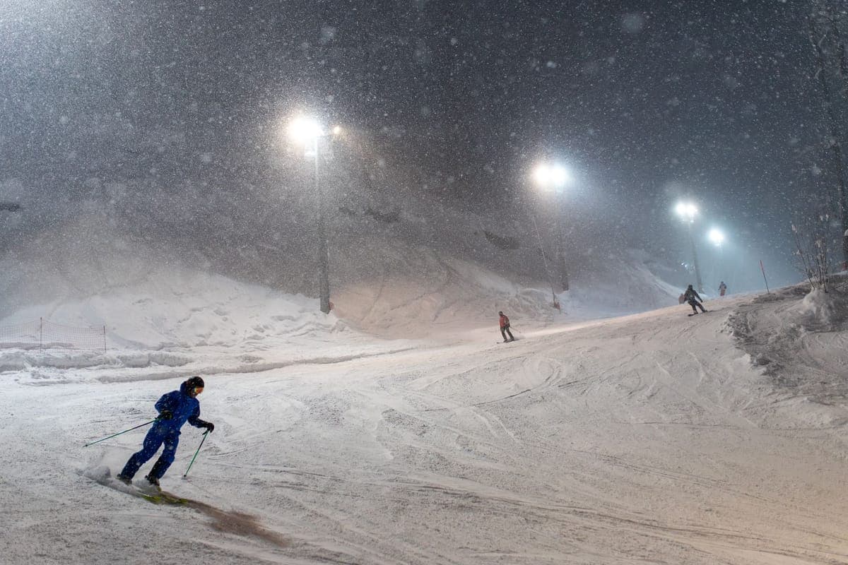 Skiers on a floodlit snow-covered slope on a clear winter night