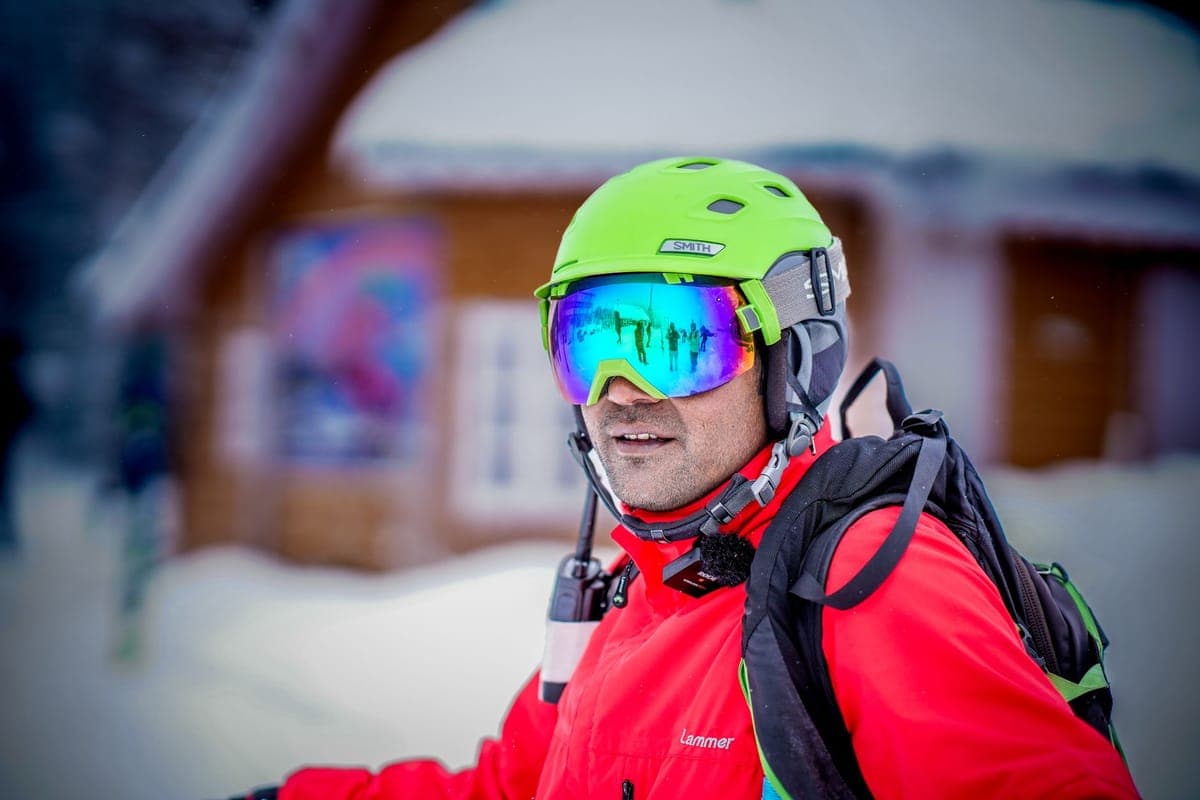 Adult skier wearing a helmet and reflective goggles on a snowy slope