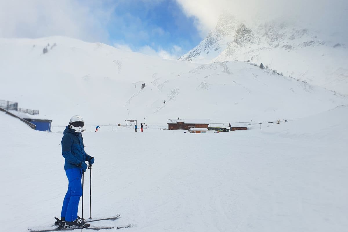 A skier pausing to look at snow-capped mountains under a clear sky