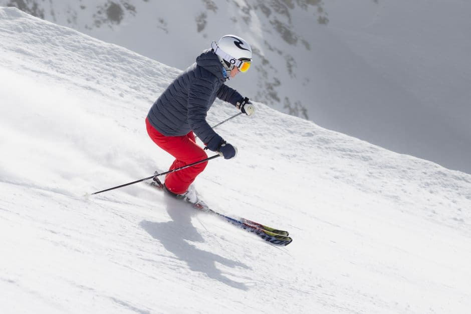 A skier in red pants descending a snowy mountain slope on a bright day