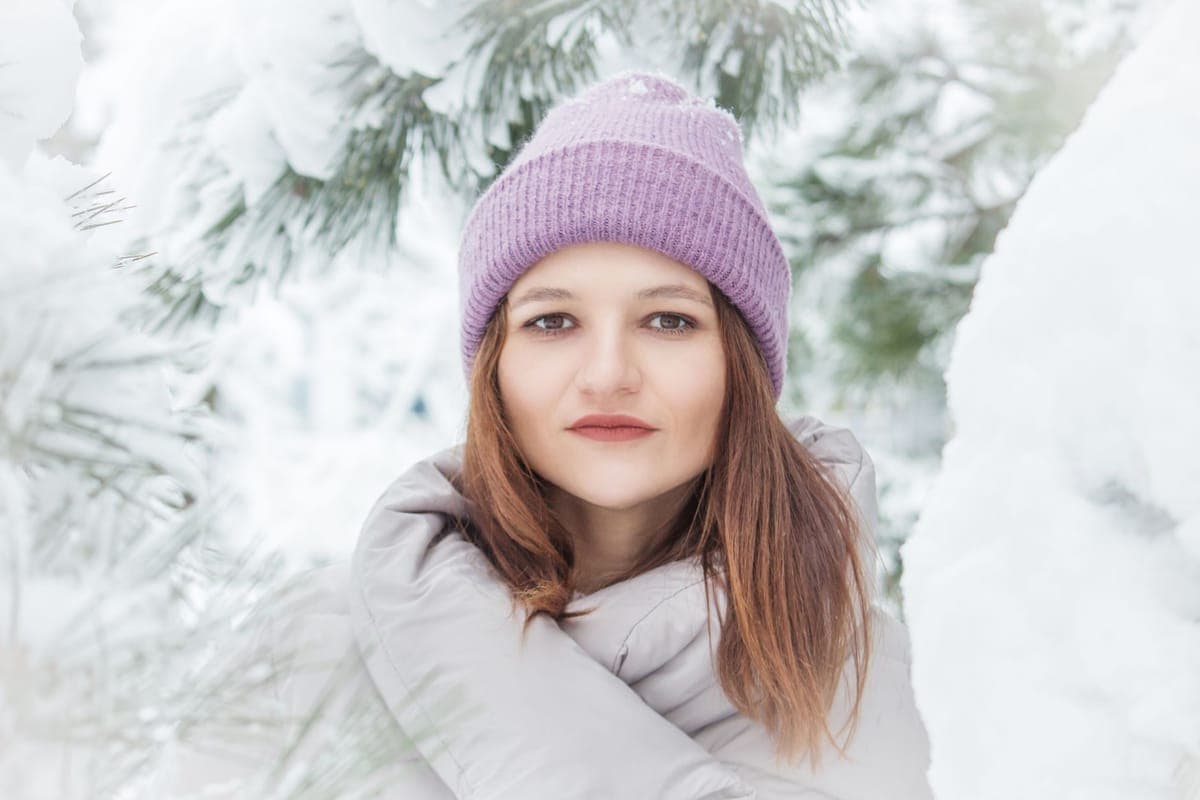 A person wearing a knitted beanie in a snowy winter forest