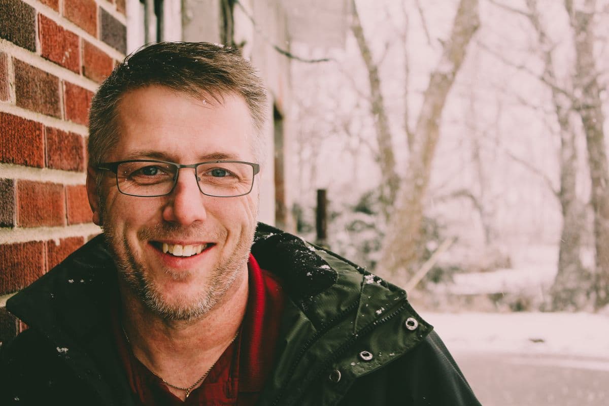 A smiling man wearing eyeglasses and a winter coat outdoors in the snow