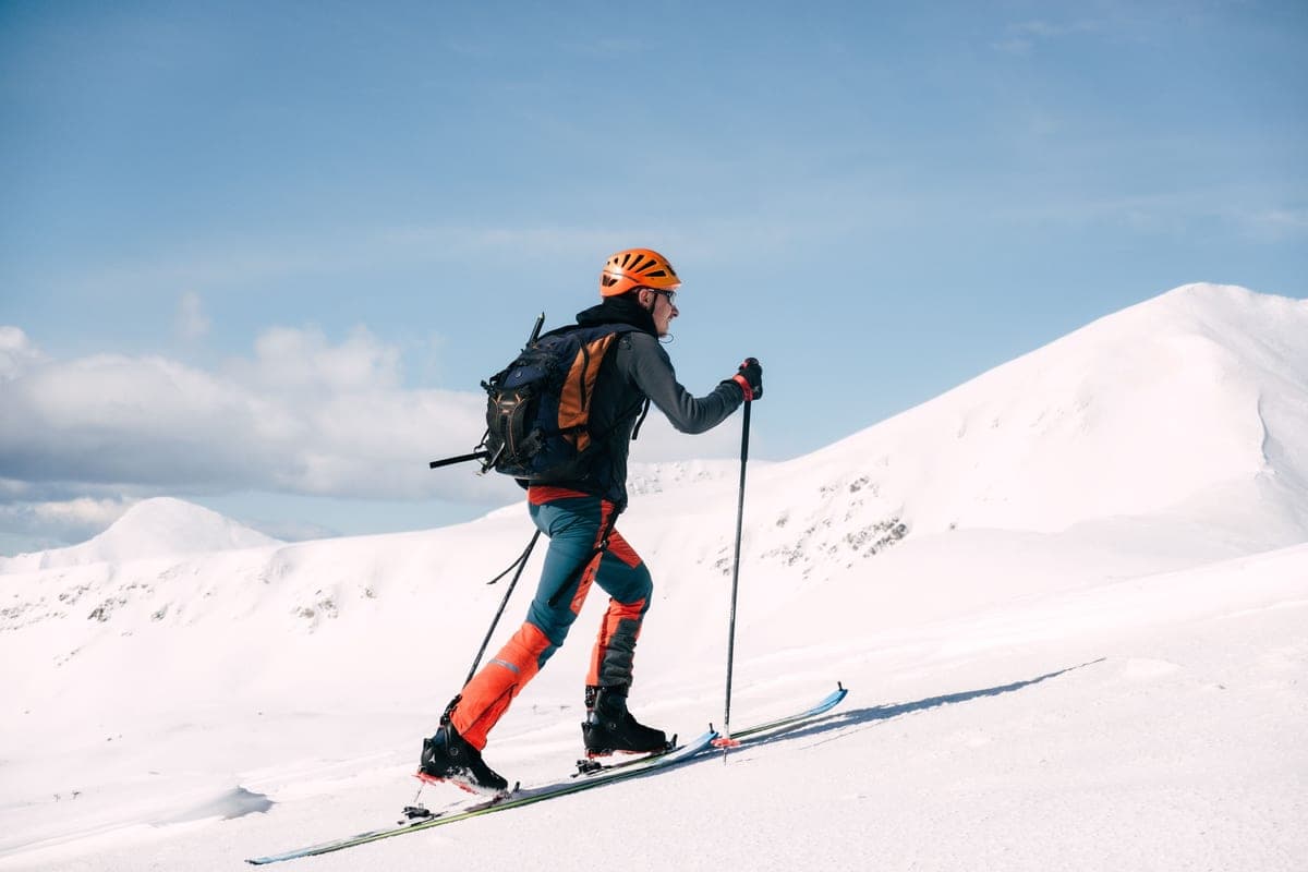 A skier climbing a snowy mountain in bright gear under a clear sky