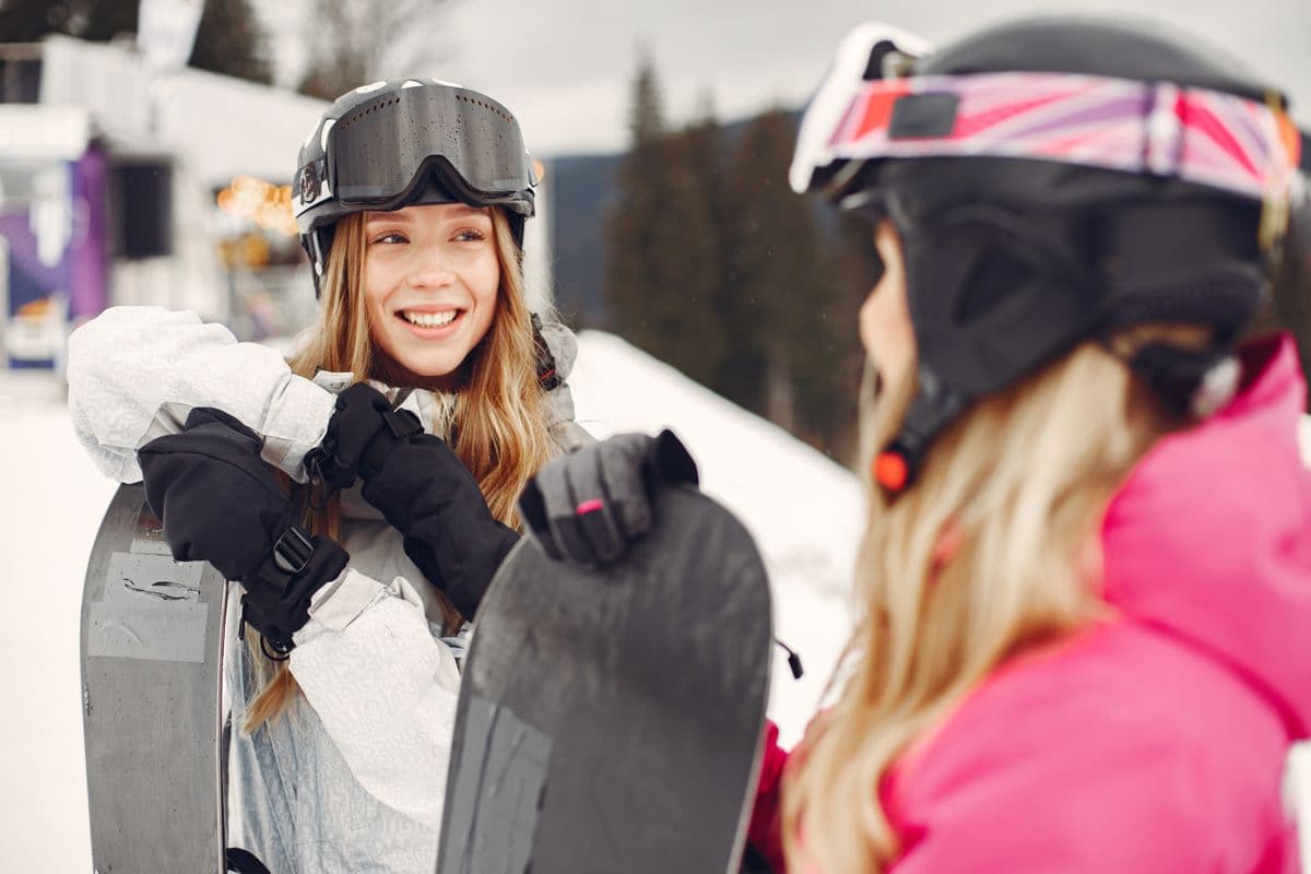 Two young women with snowboards on a snowy mountain on a clear day