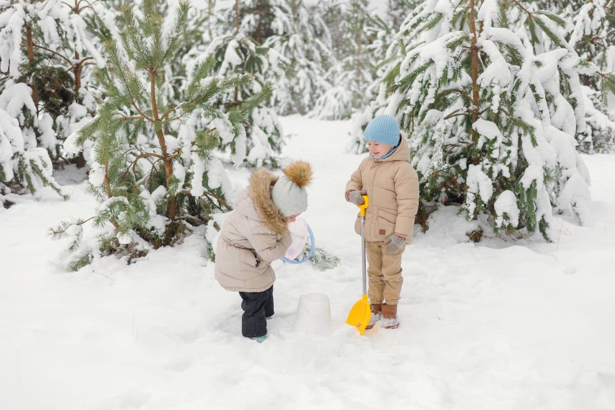 Two children playing with a shovel in a snowy winter forest
