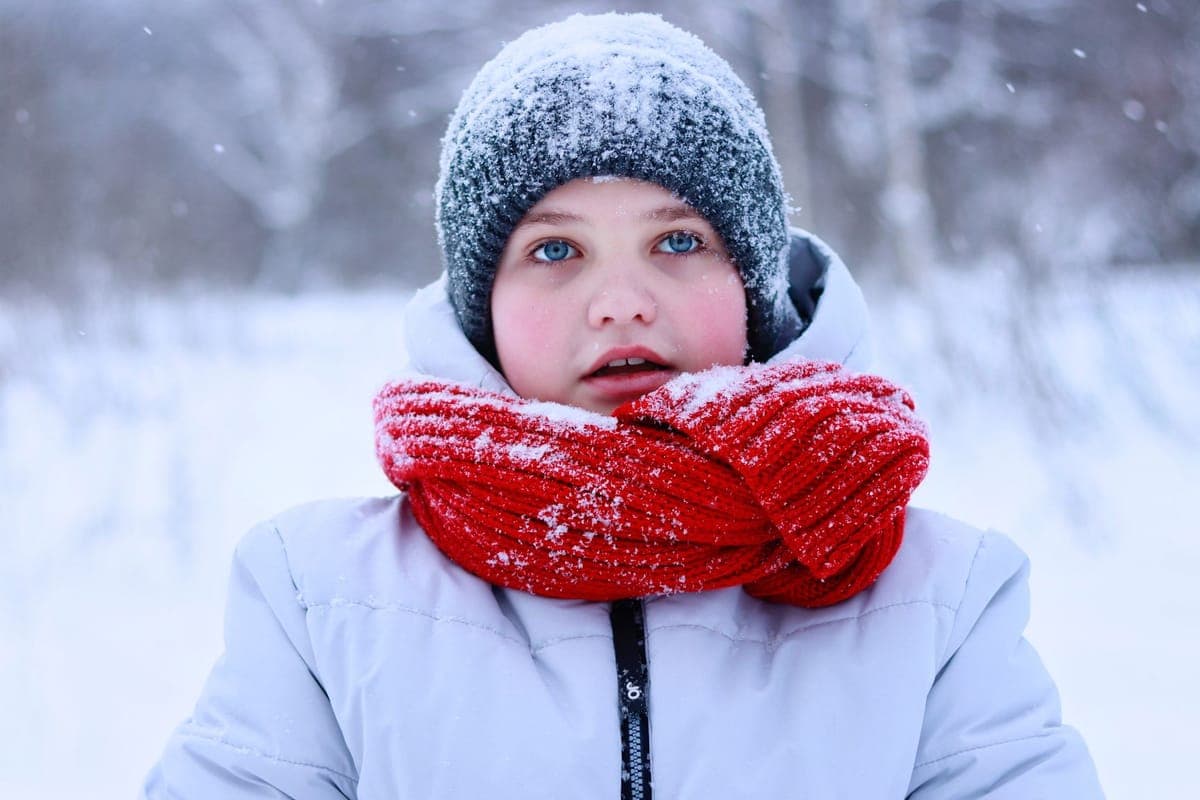 A child in winter clothing with a red scarf as snow falls around them