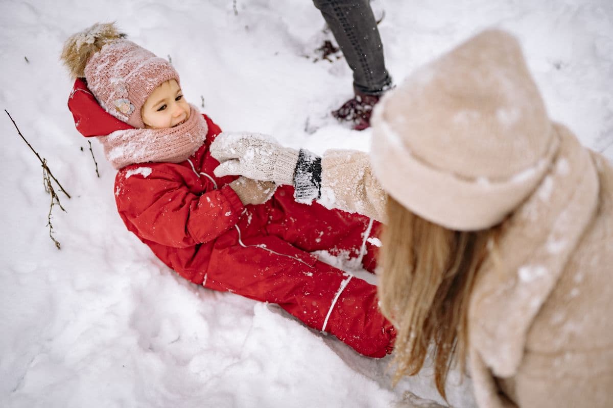 A child dressed warmly in winter clothes playing in the snow with family nearby