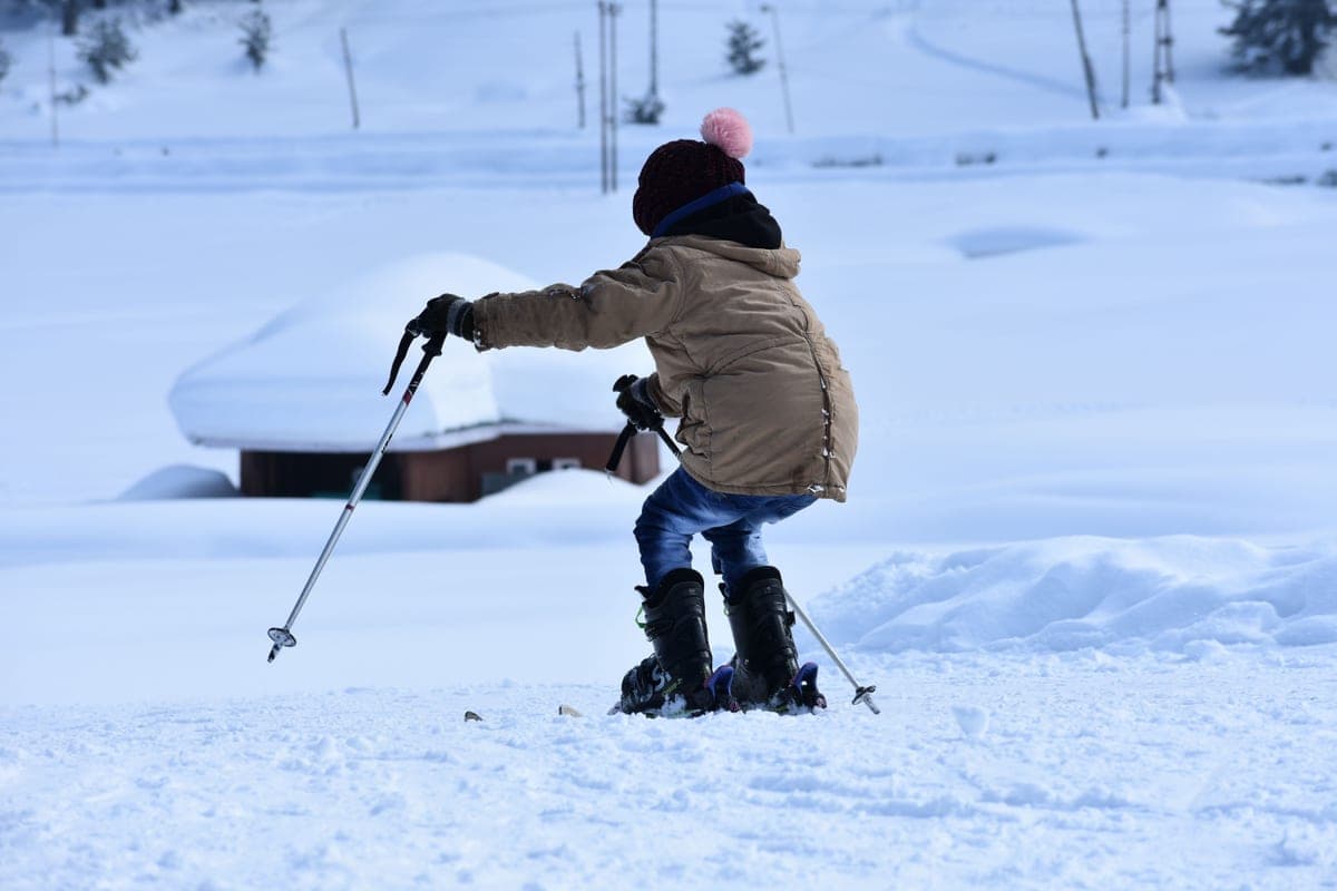 A young child learning to ski on a snowy slope on a bright winter day