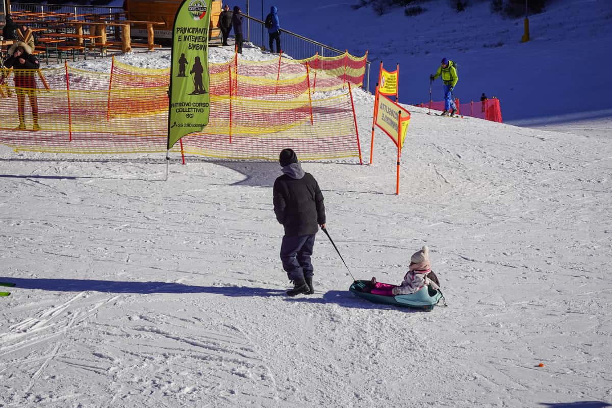 A parent pulling a child on a sled at a snowy ski resort
