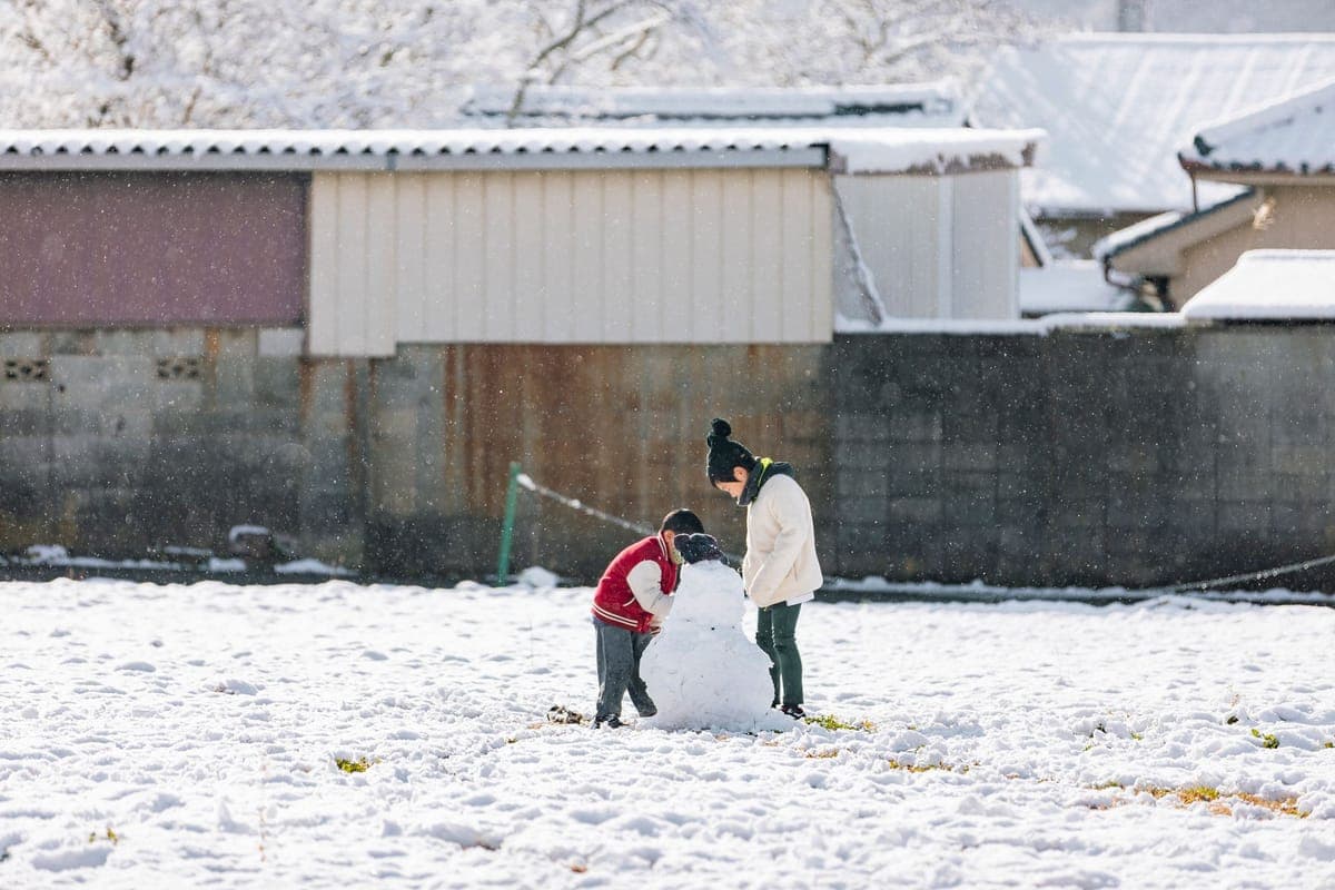 Two children building a snowman in a snowy field on a winter day