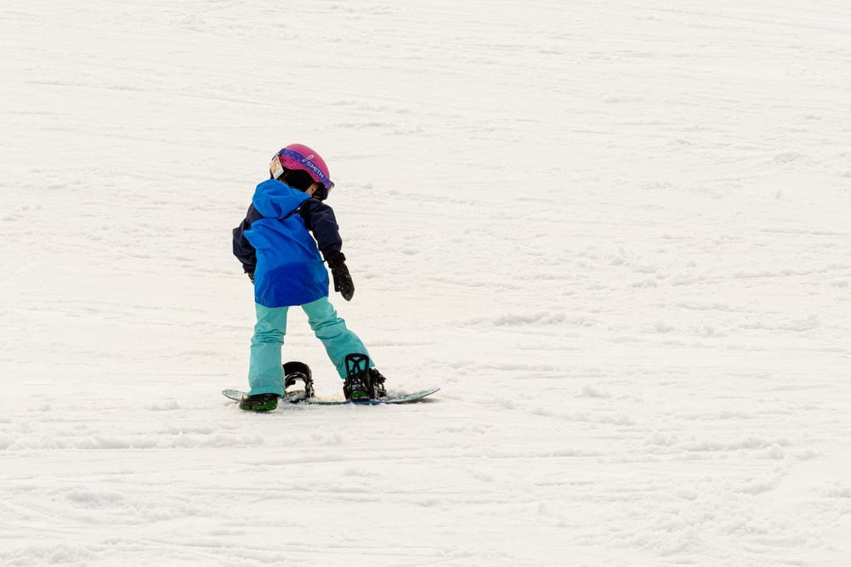 Young child learning to snowboard on a snowy slope in bright winter gear