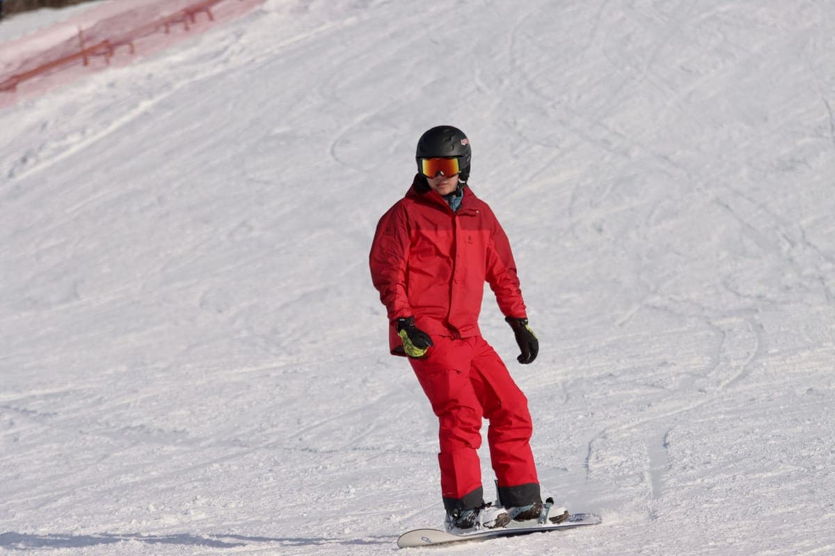A teenager in bright winter gear snowboarding on a snowy slope