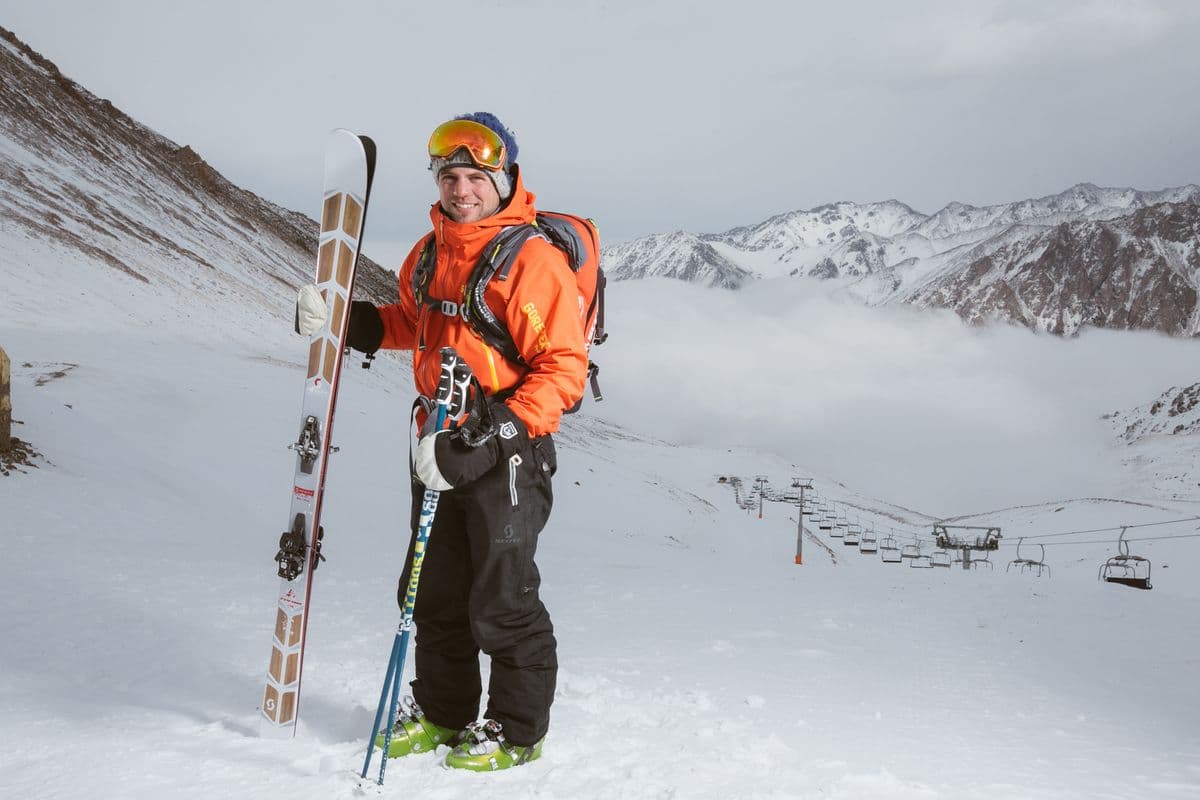 A smiling skier in an orange jacket on a snowy mountain with skis