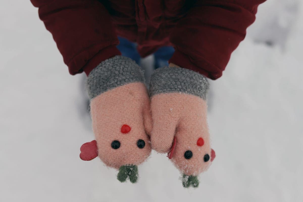 A child's hands in mittens outdoors during winter snowfall