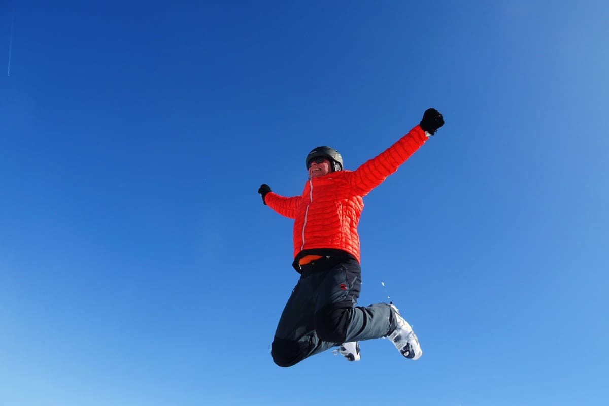 A skier leaping midair against a clear blue sky in ski gear
