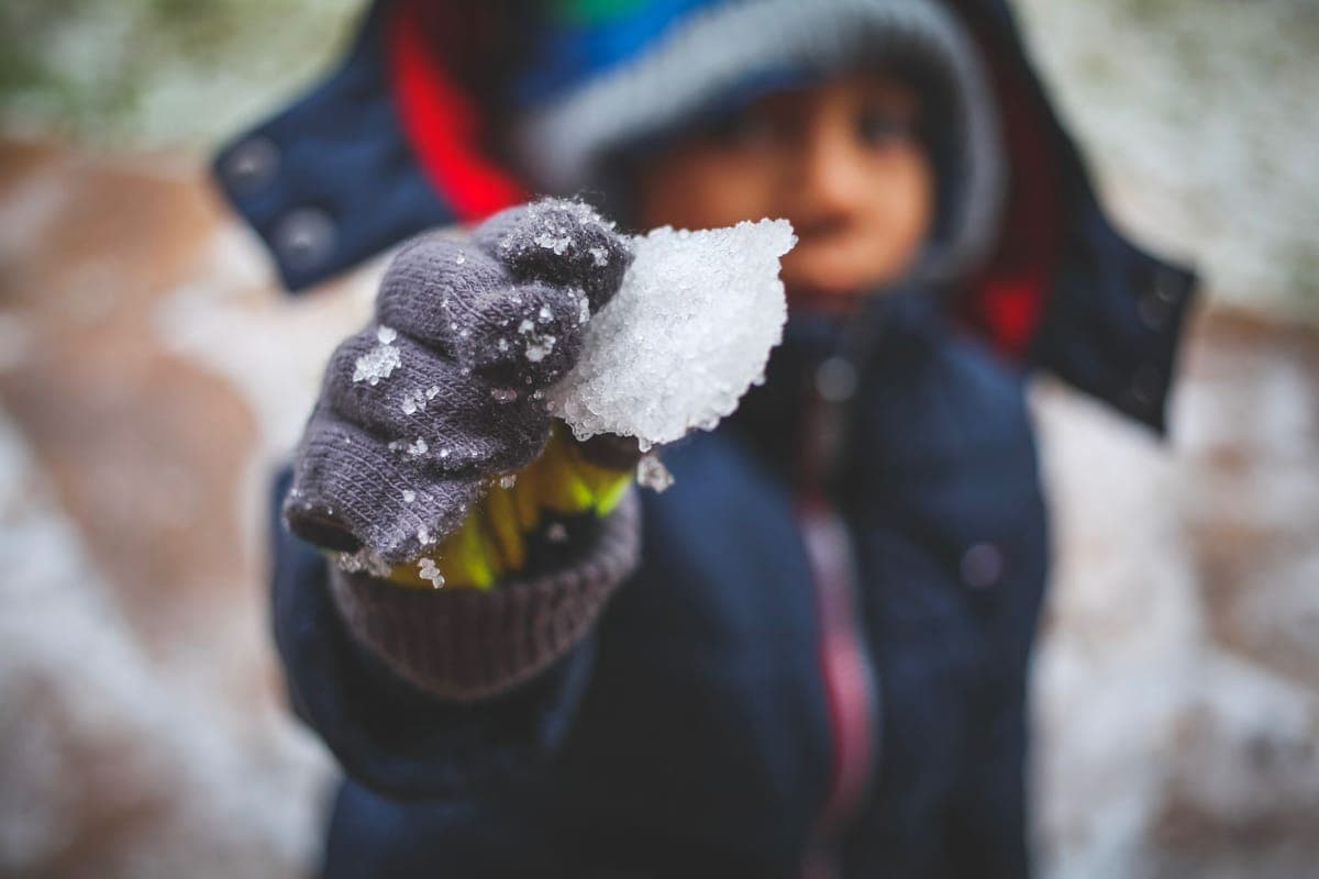 A child in winter clothing holding a handful of snow in a mittened hand