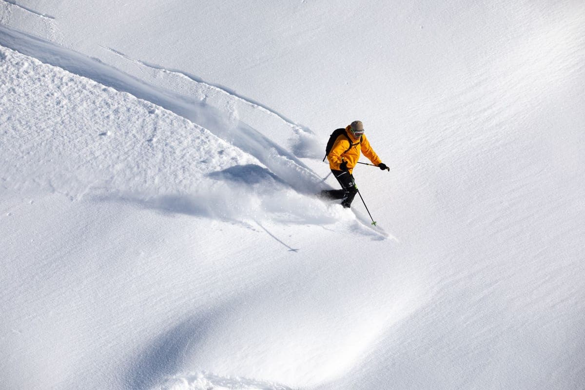 A skier in a yellow jacket descending a snowy slope on a bright day