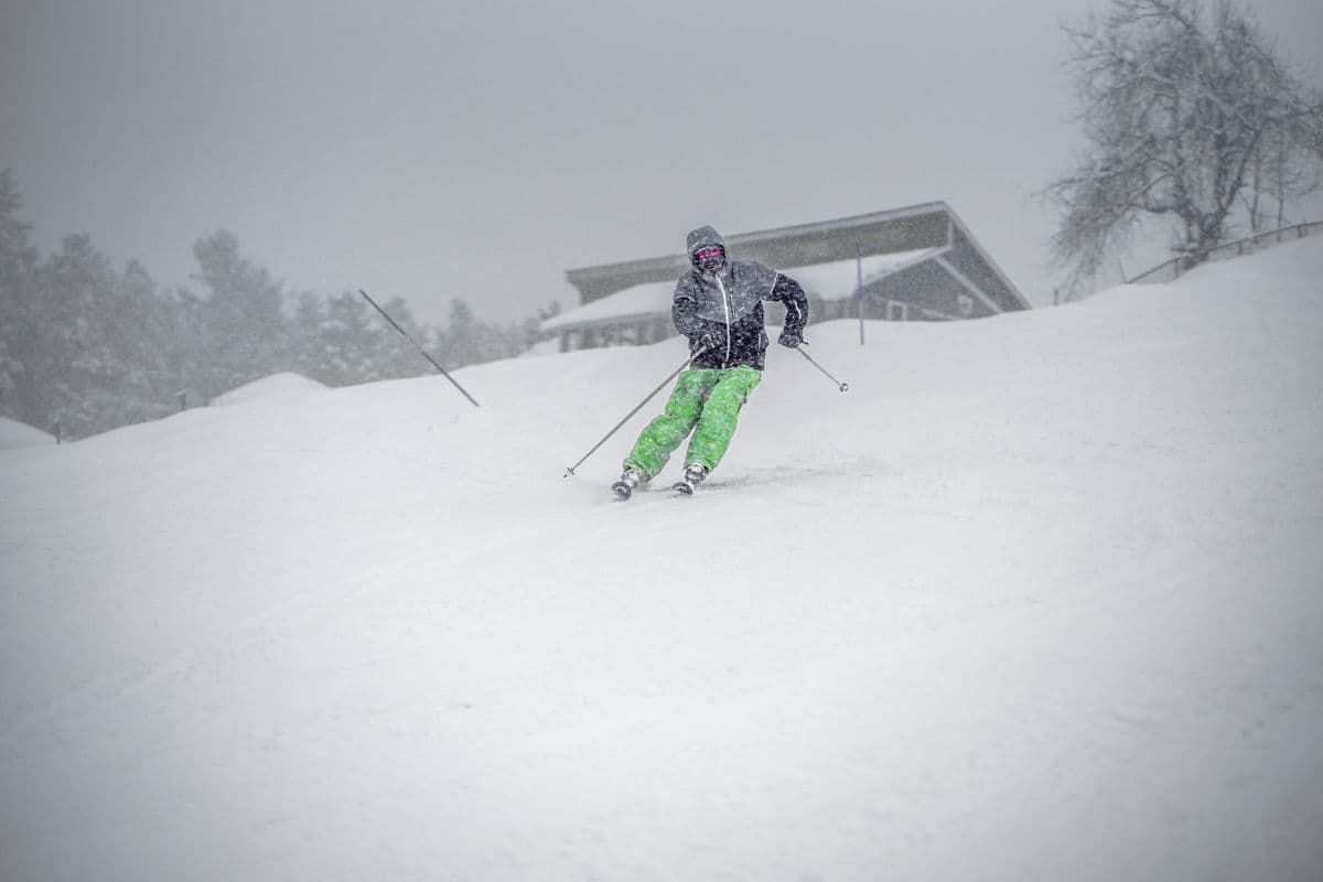 A skier in bright green pants skiing downhill in wet snowy weather