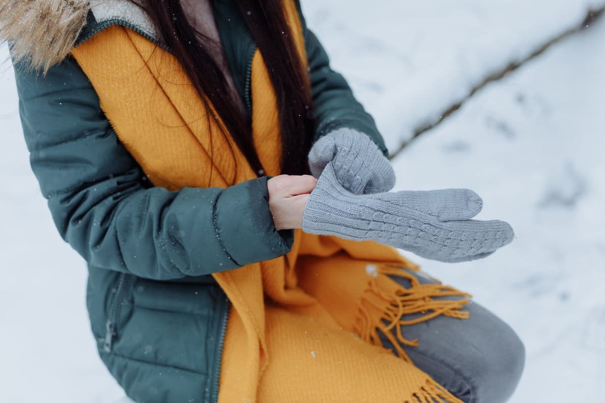Close-up of a person in a winter coat adjusting gloves in the snow