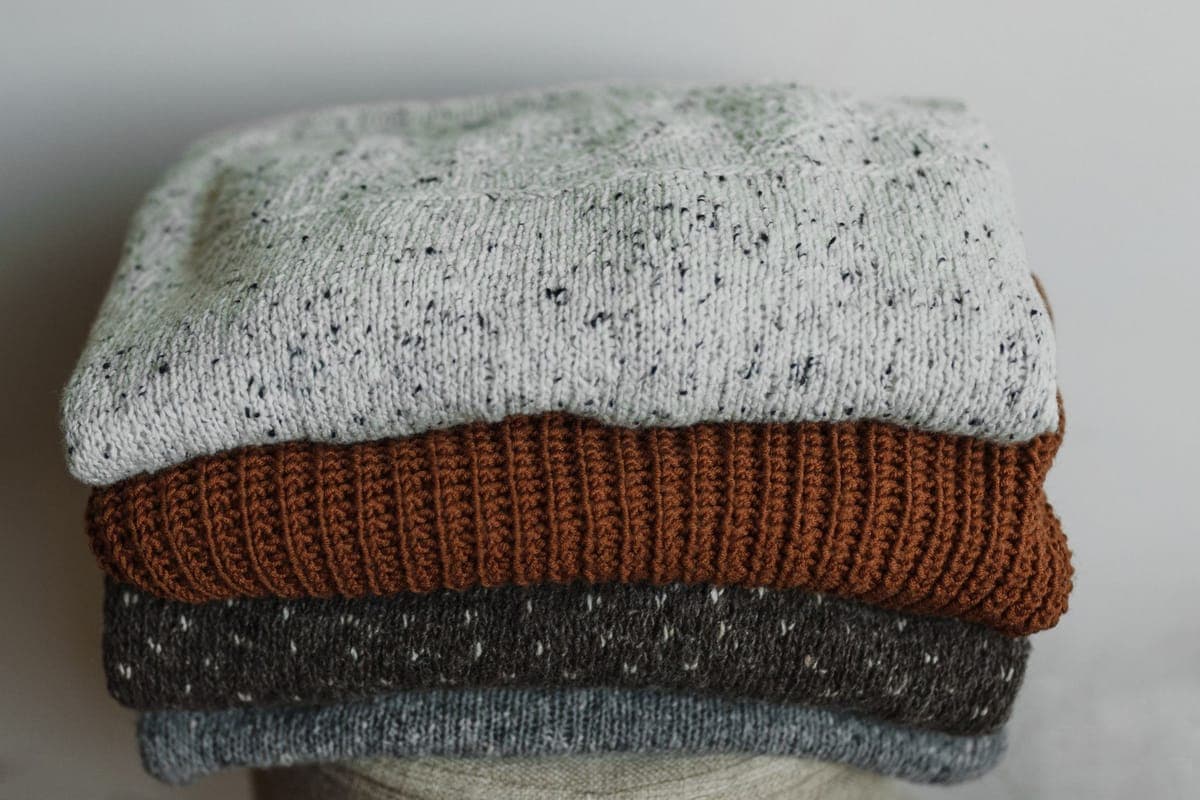 Folded knitted winter garments in neutral tones stacked closely together