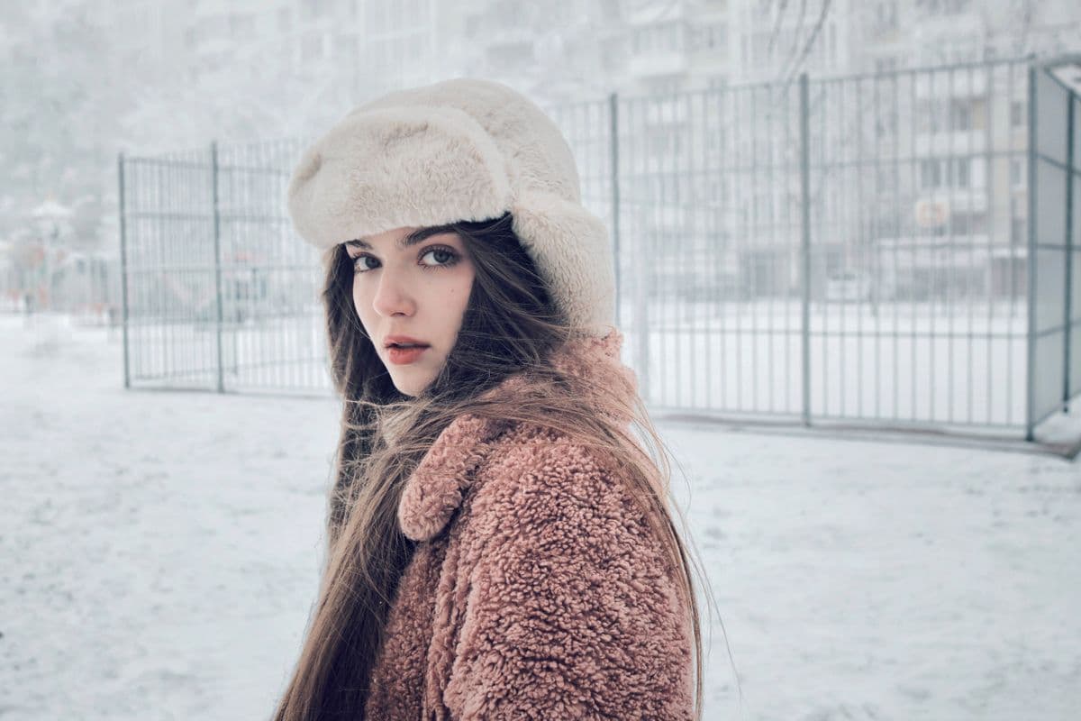 A young woman in everyday winter clothes standing outdoors in a snowy urban street