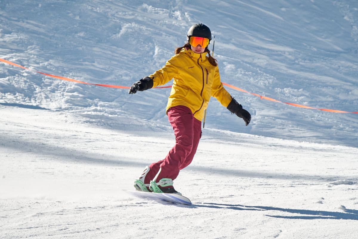 A snowboarder in a yellow jacket riding down a sunny snowy slope