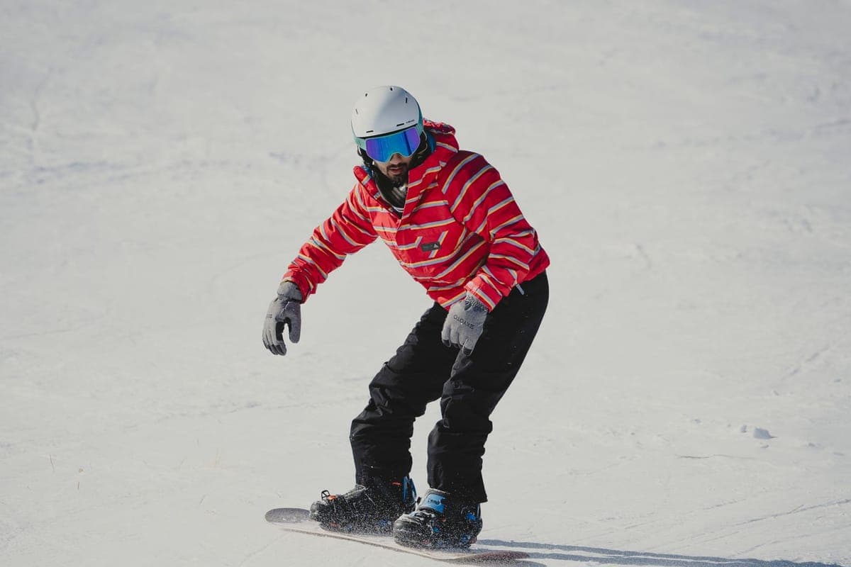 A snowboarder in a red jacket riding down a snowy slope