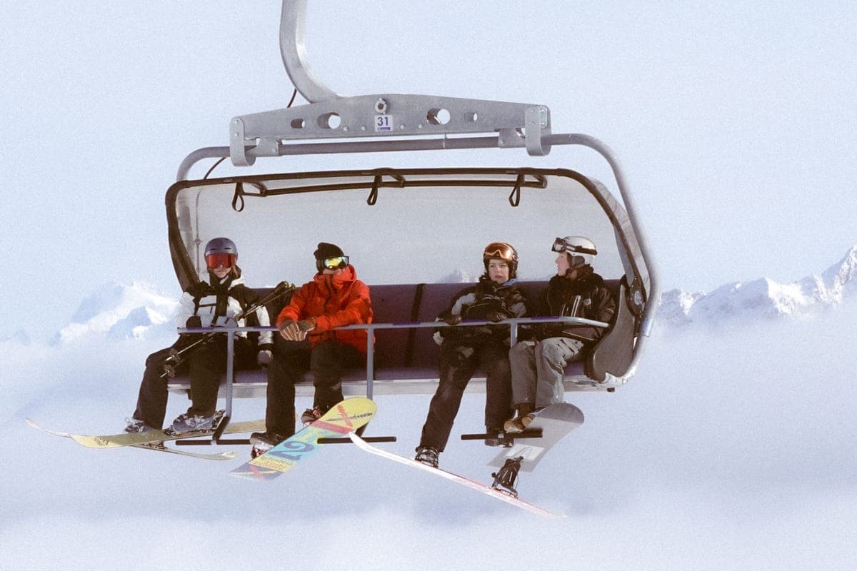 Four people riding a chairlift above snowy alpine slopes in winter